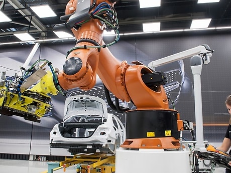 Einbau der Batterie in ein Hybridfahrzeug. Durch Mensch-Roboter-Kooperation (MRK) und den Einsatz eines Fahrerlosen Transportfahrzeugs (FTF) wird die Montage flexibler.