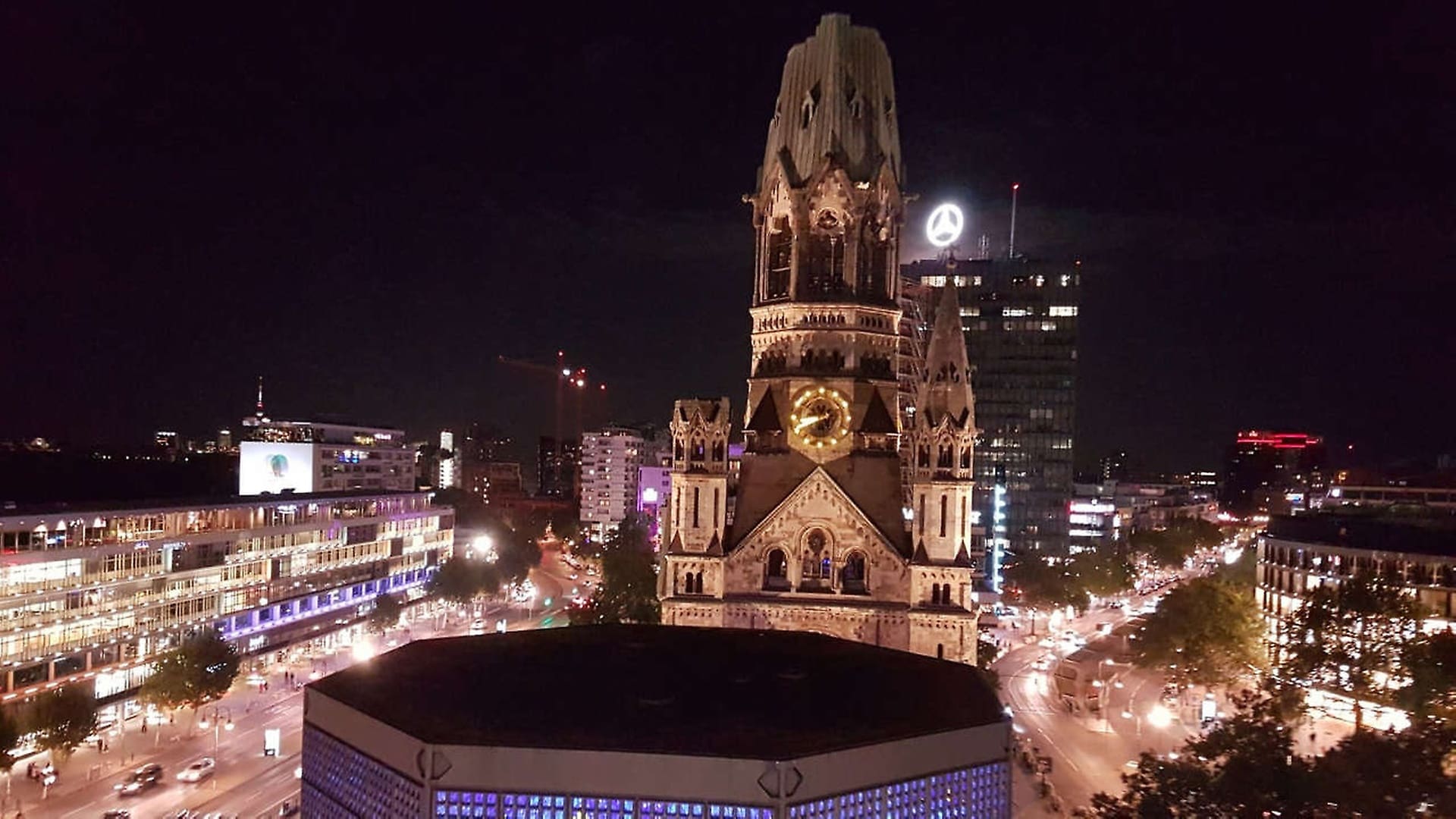 The Mercedes Star in Berlin shines behind the The Kaiser Wilhelm Memorial Church