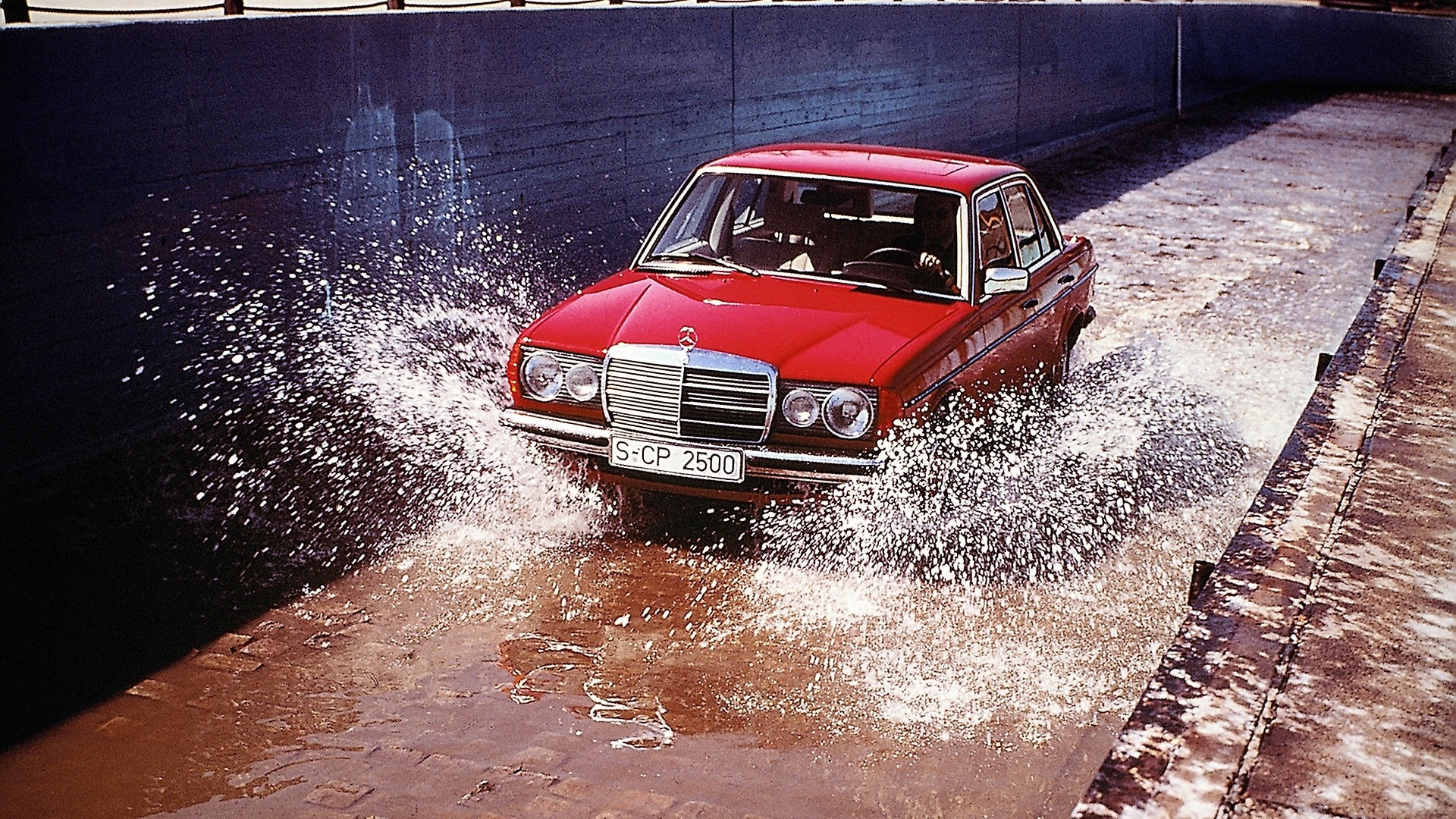A Mercedes-Benz 123-series Saloon drives through a water basin on the test track.