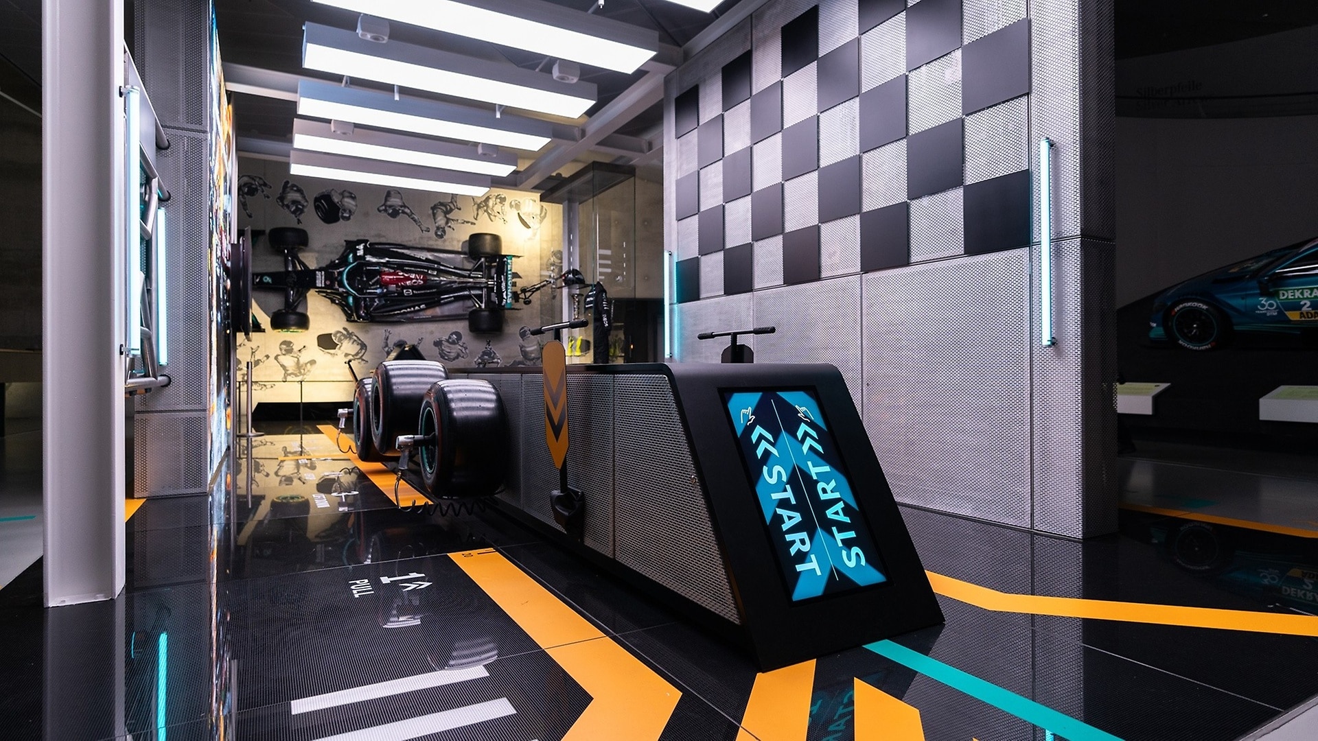 In this interactive game, real Formula 1 wheels are changed against the clock. In the background, a 2021 Mercedes-AMG F1 W12 E Performance Formula 1 racing car hanging vertically on the wall. 